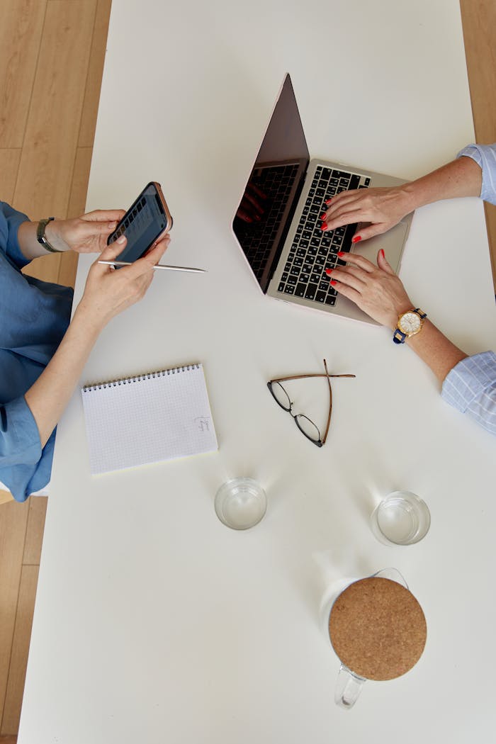 Two businesswomen collaborating in an office with laptop and smartphone.